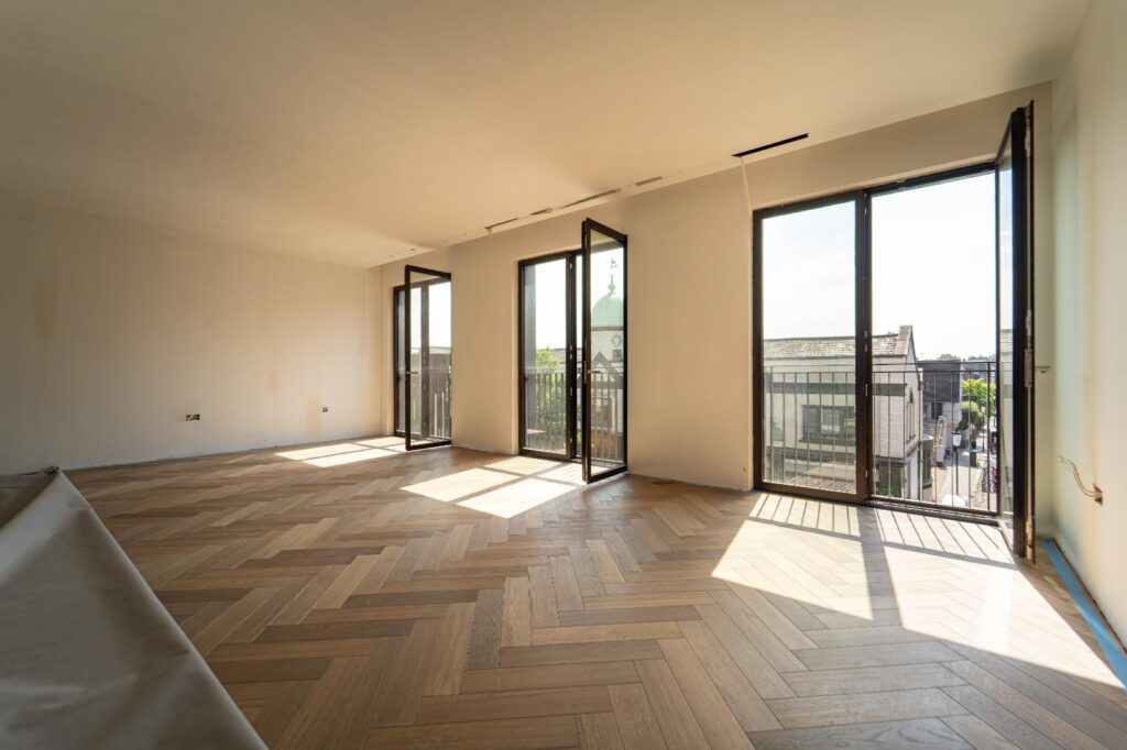 3 large patio doors of a high-rise building opened up with sunlight on the newly laid parquet wood flooringwood