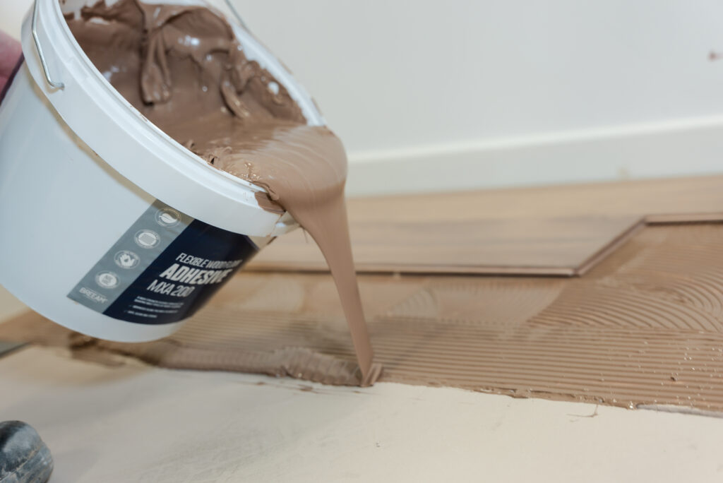 Wood adhesive being poured from white container onto wooden surface