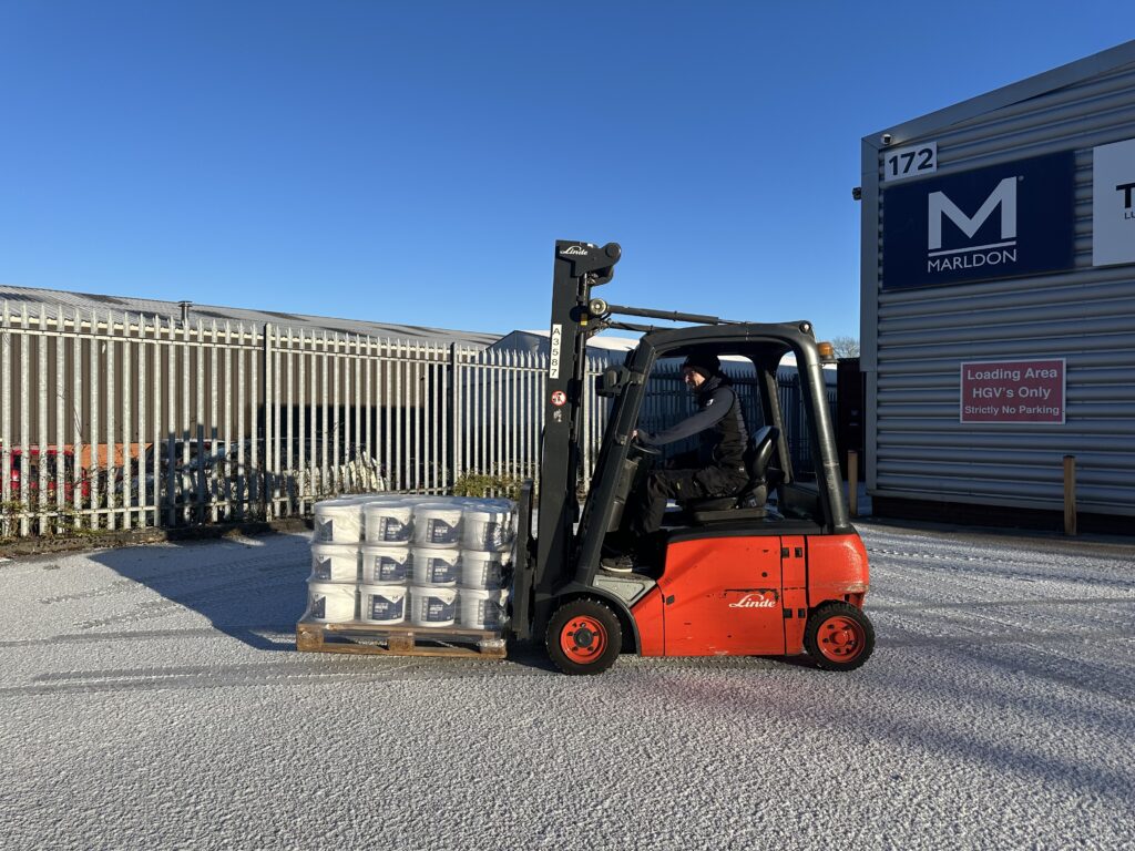 Red Linde forklift loading palletted goods at industrial warehouse